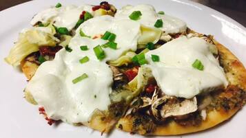 A plate of food with a white sauce, green onions, and pieces of meat on a flatbread base.