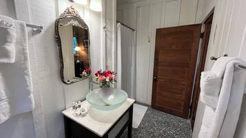 A bathroom with a glass sink, a mirror with an ornate frame, and a wooden door.