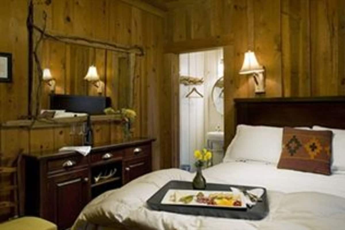 A wooden room with a bed, bedside table, lamp, and a small table with a tray of food.