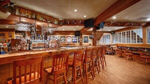 A bar area with wooden bar stools, a variety of liquor bottles, and framed sports jerseys on the wall. - Best Western Plus Windjammer Inn & Conference Center (South Burlington)
