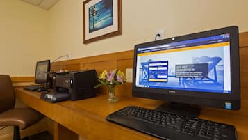 A hotel reception desk with a desktop computer, a printer, and a keyboard. There is a framed picture on the wall above the desk.