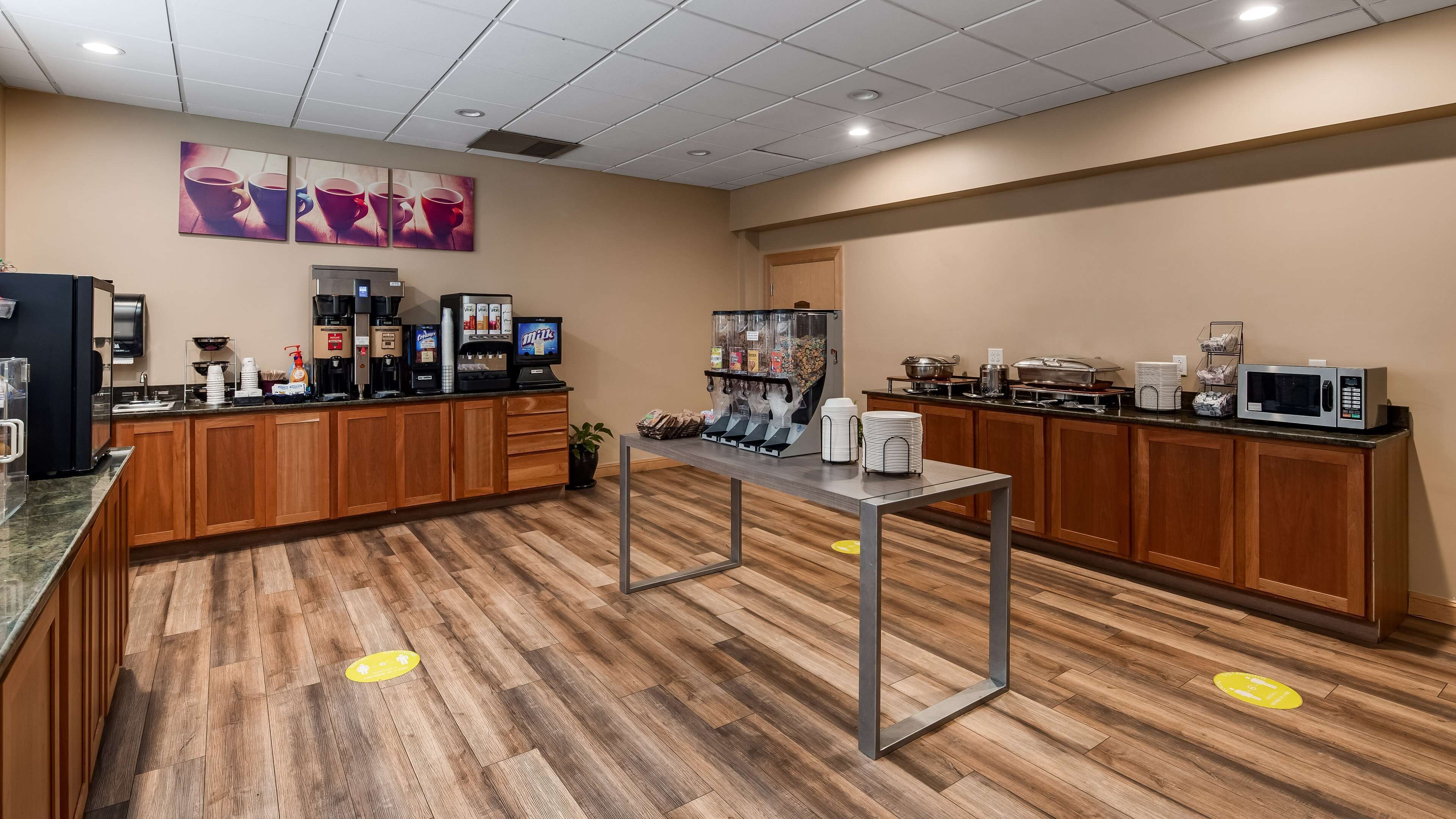 A modern kitchen area with wooden cabinets, a coffee station, a microwave, and a beverage dispenser.