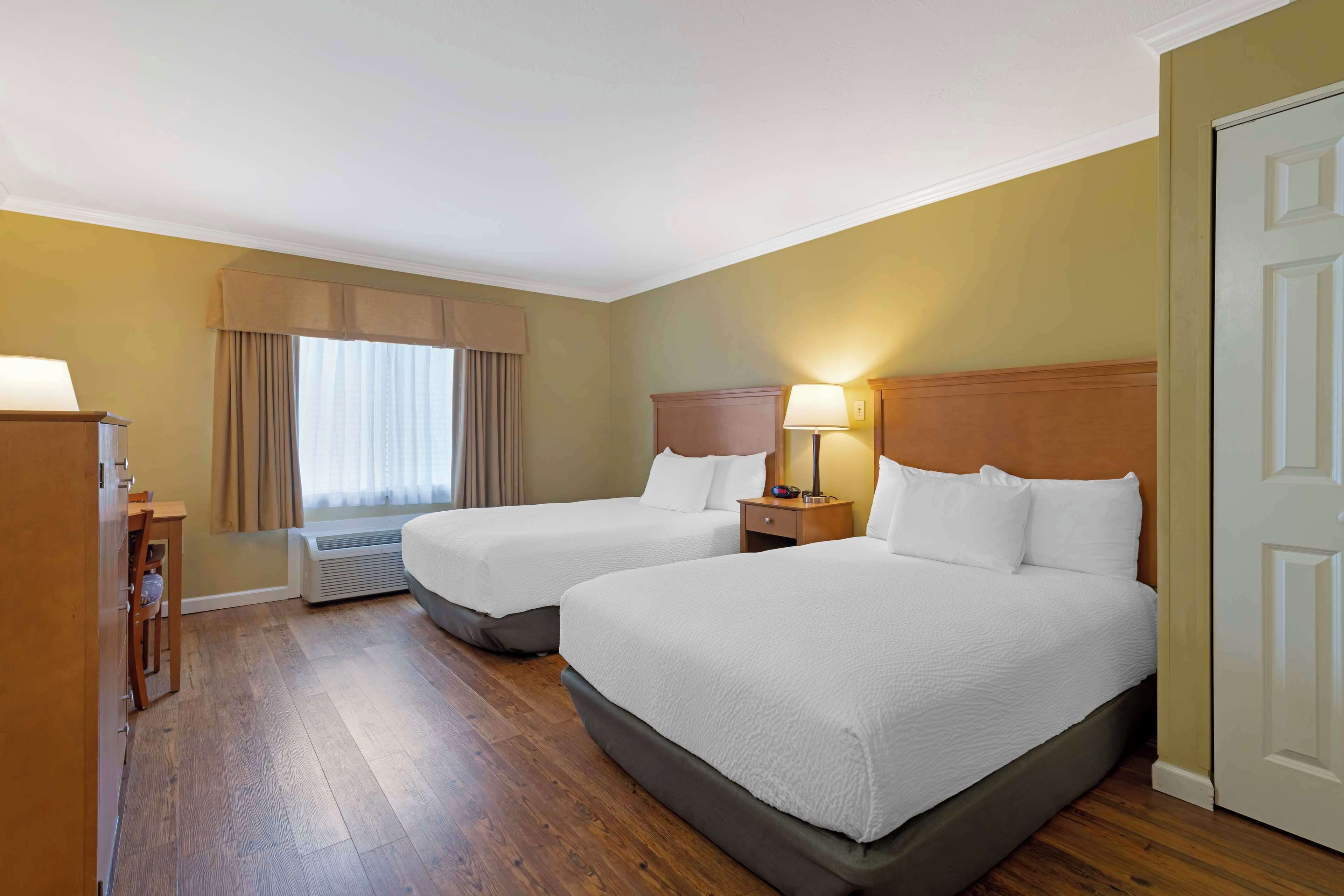 A hotel room with two beds, a desk, a chair, a lamp, and a window with curtains.