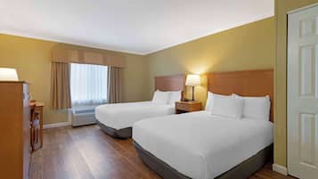 A hotel room with two beds, a desk, a chair, a lamp, and a window with curtains.