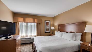Habitación de hotel con una cama grande, televisor, escritorio y ventana con cortinas.
