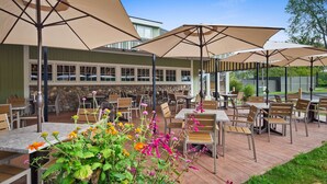 An outdoor patio with tables and chairs, large umbrellas, and a stone wall in the background. - Best Western Plus Windjammer Inn & Conference Center (South Burlington)