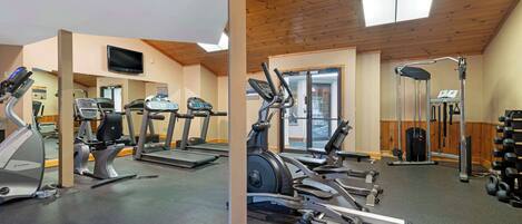 A gym with various exercise equipment, a television, and a window with a view of the outside.
