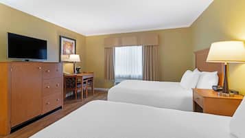 A hotel room with two beds, a desk with a chair, a television, and a lamp.