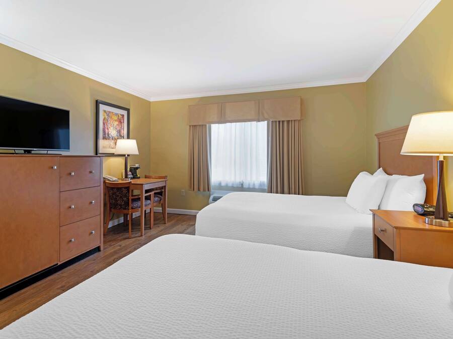 A hotel room with two beds, a desk with a chair, a television, and a lamp.