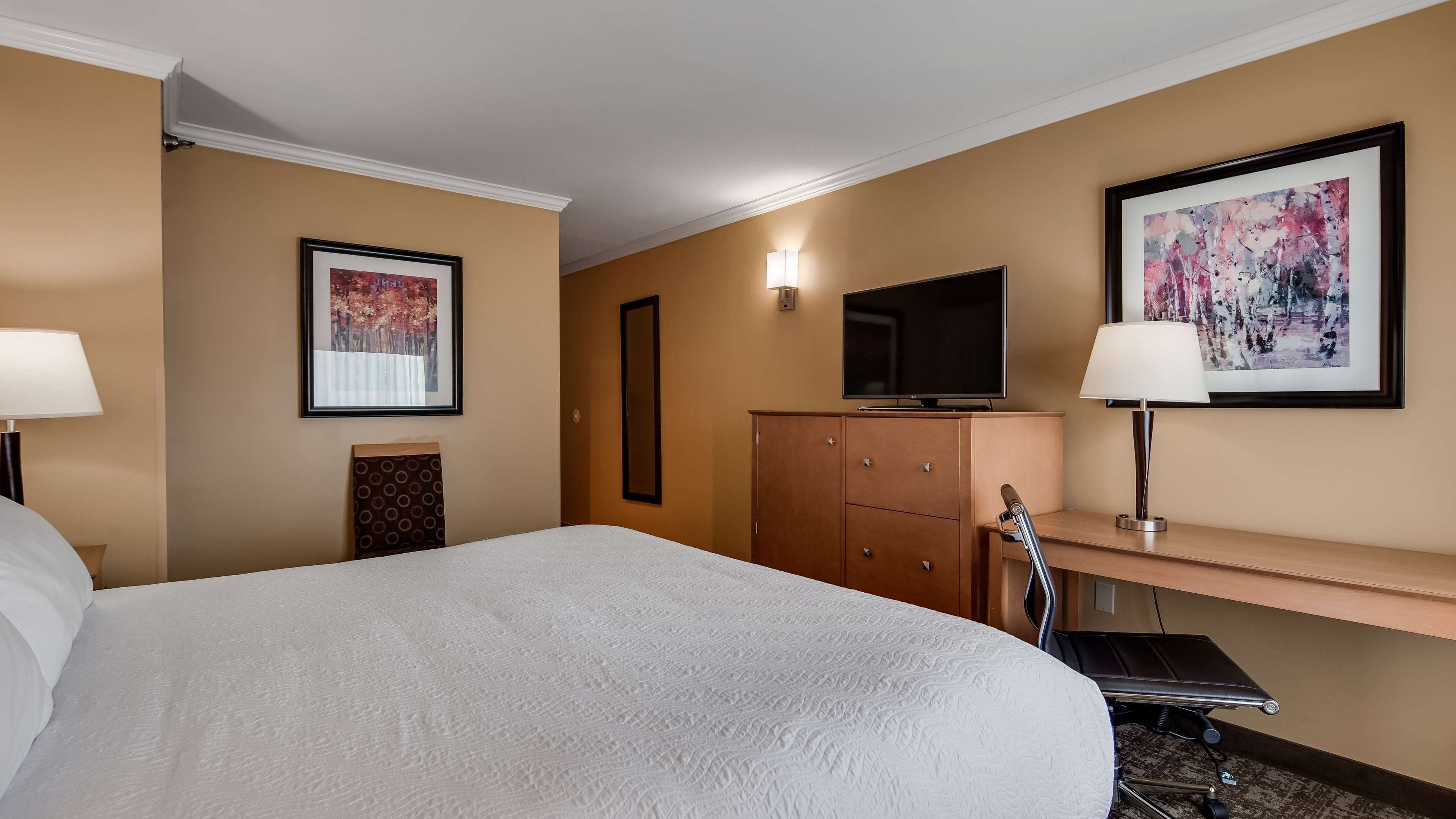 Een hotelkamer met een groot bed, een bureau met stoel, een televisie en twee kunstwerken in lijsten aan de muur.
