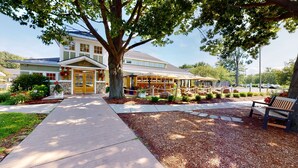 A building with a large tree in front, a covered outdoor seating area, and a pathway leading to the entrance. - Best Western Plus Windjammer Inn & Conference Center (South Burlington)