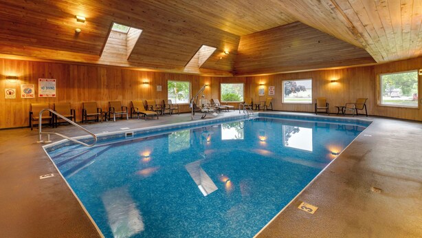 An indoor swimming pool with wooden walls and ceiling, multiple windows, and a pool ladder. - Best Western Plus Windjammer Inn & Conference Center (South Burlington)