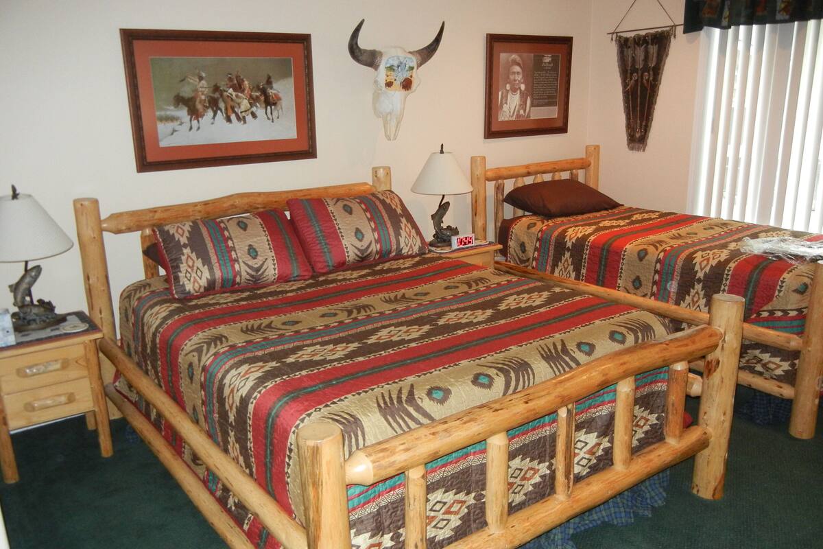 Una cama de madera con colcha estampada, una mesita de noche con lámpara y un reloj en la pared.