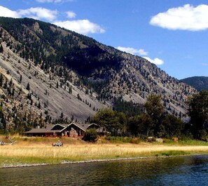 A cabin with a large deck, surrounded by a forested mountain backdrop.