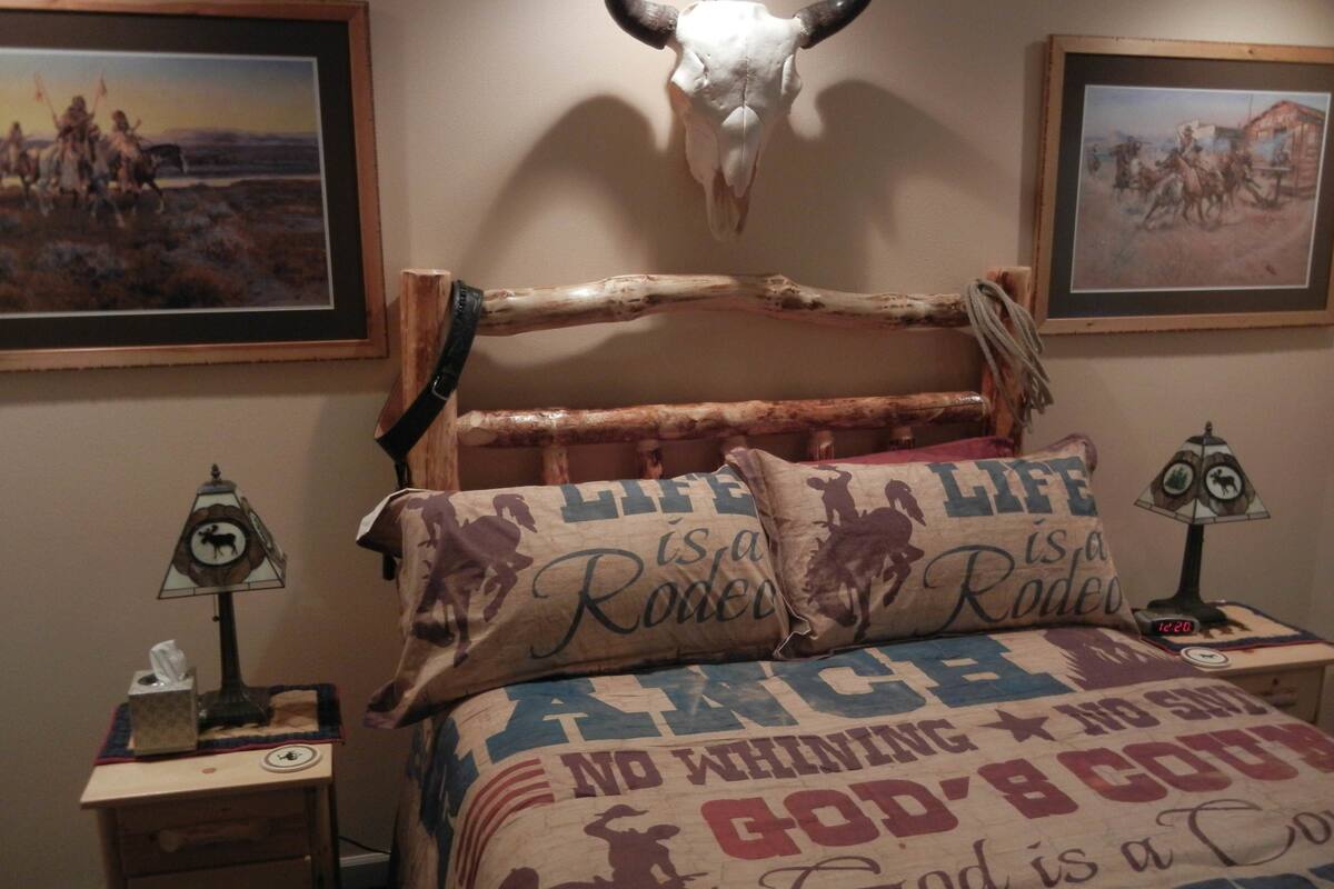 Un dormitorio de estilo rústico, con un cráneo de vaca en la pared, almohadas con motivos vaqueros y una colcha con diseños de vaquero.