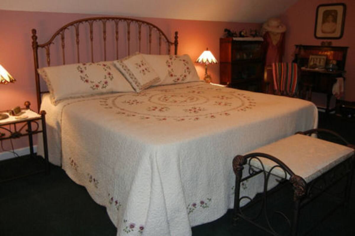 Un dormitorio con cama con dosel, una mesita de noche con lámpara y un banco al pie de la cama.