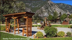 Een houten prieel met een bank, een stenen fontein en een berg op de achtergrond bij Rocky Point Ranch and Lodge.