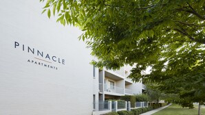 Un edificio blanco con el letrero "Pinnacle Apartments", de estilo arquitectónico moderno con balcones y un césped bien cuidado.