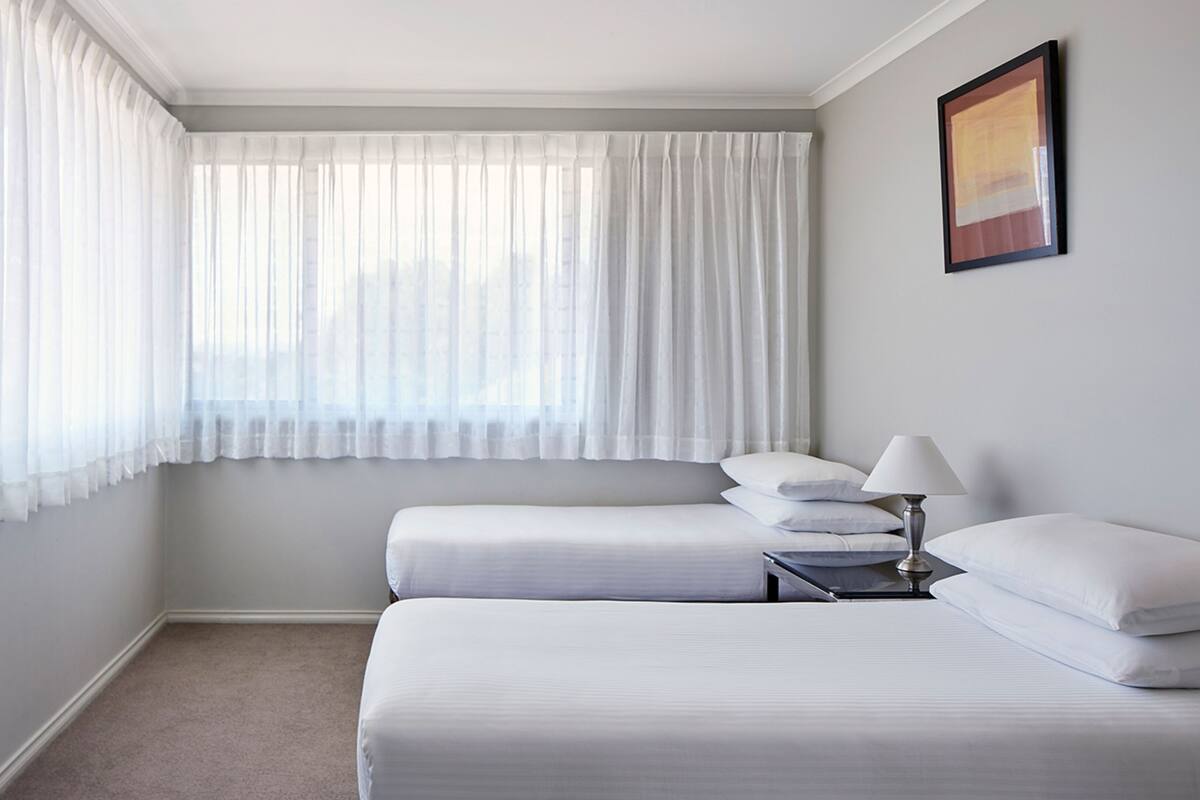Habitación de hotel con dos camas, una mesita de noche, una lámpara y un cuadro en la pared.