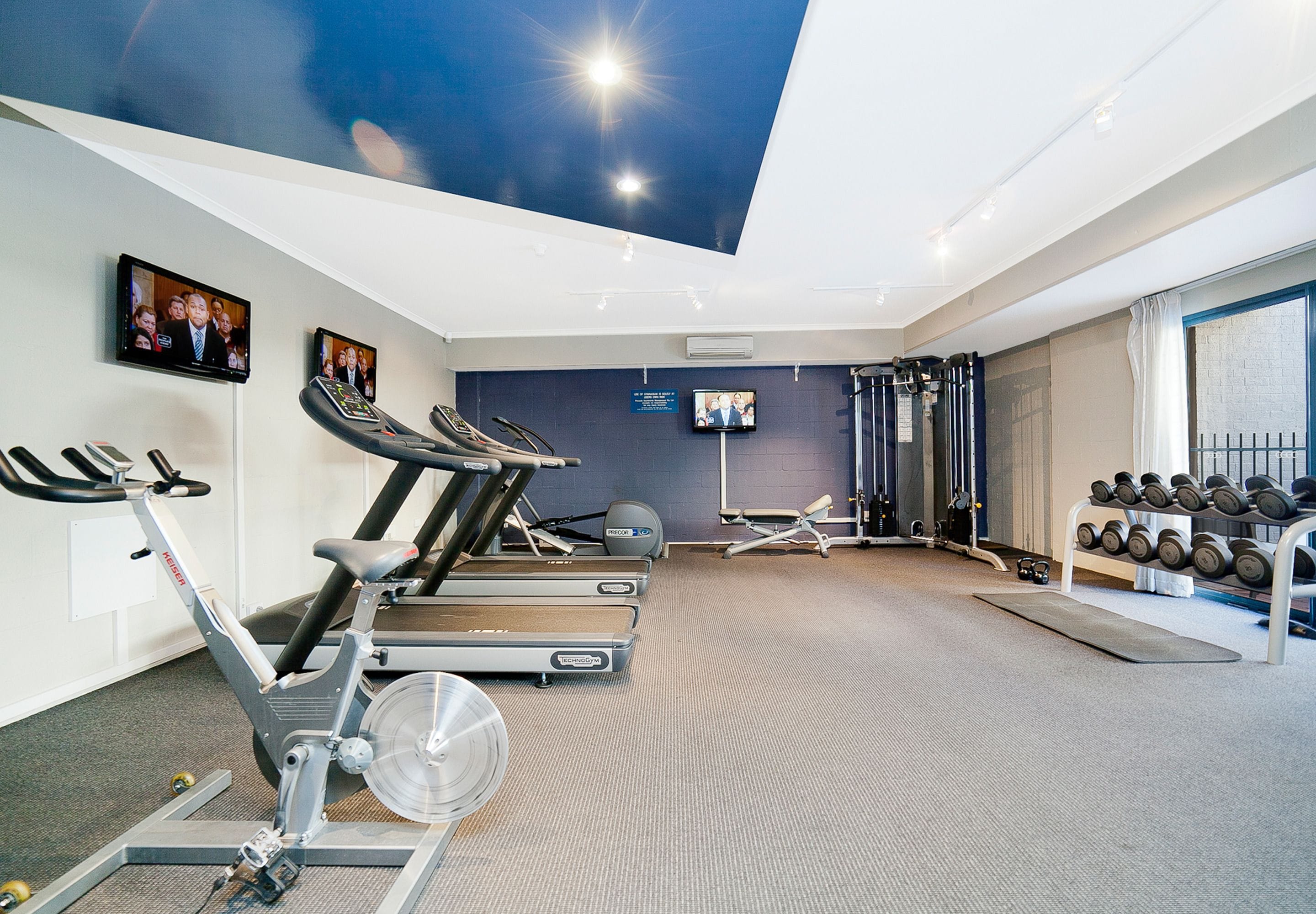 A gym with stationary bikes, treadmills, a weight rack, and a ceiling with a skylight.