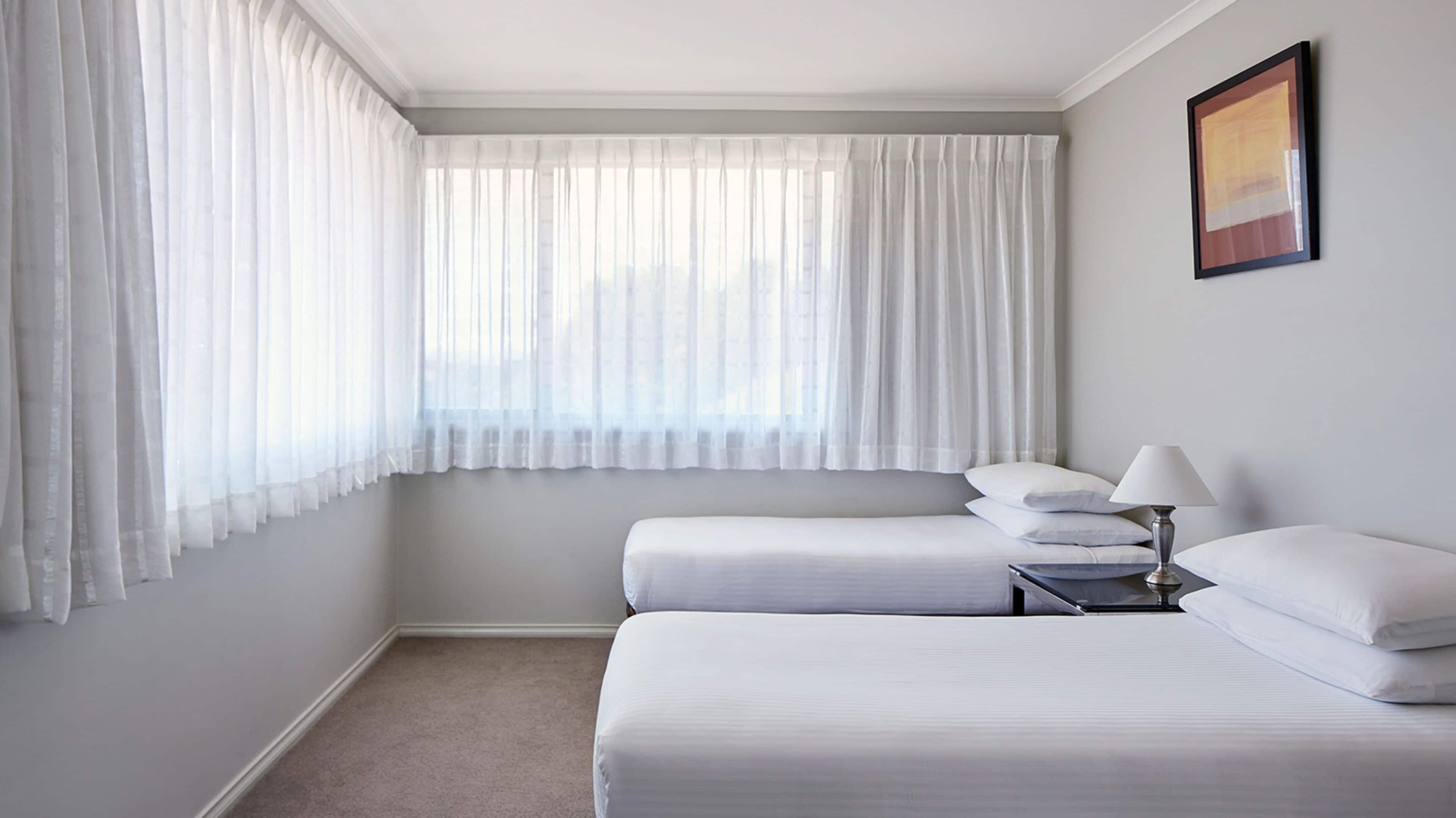 Habitación de hotel con dos camas, una mesita de noche, una lámpara y un cuadro en la pared.