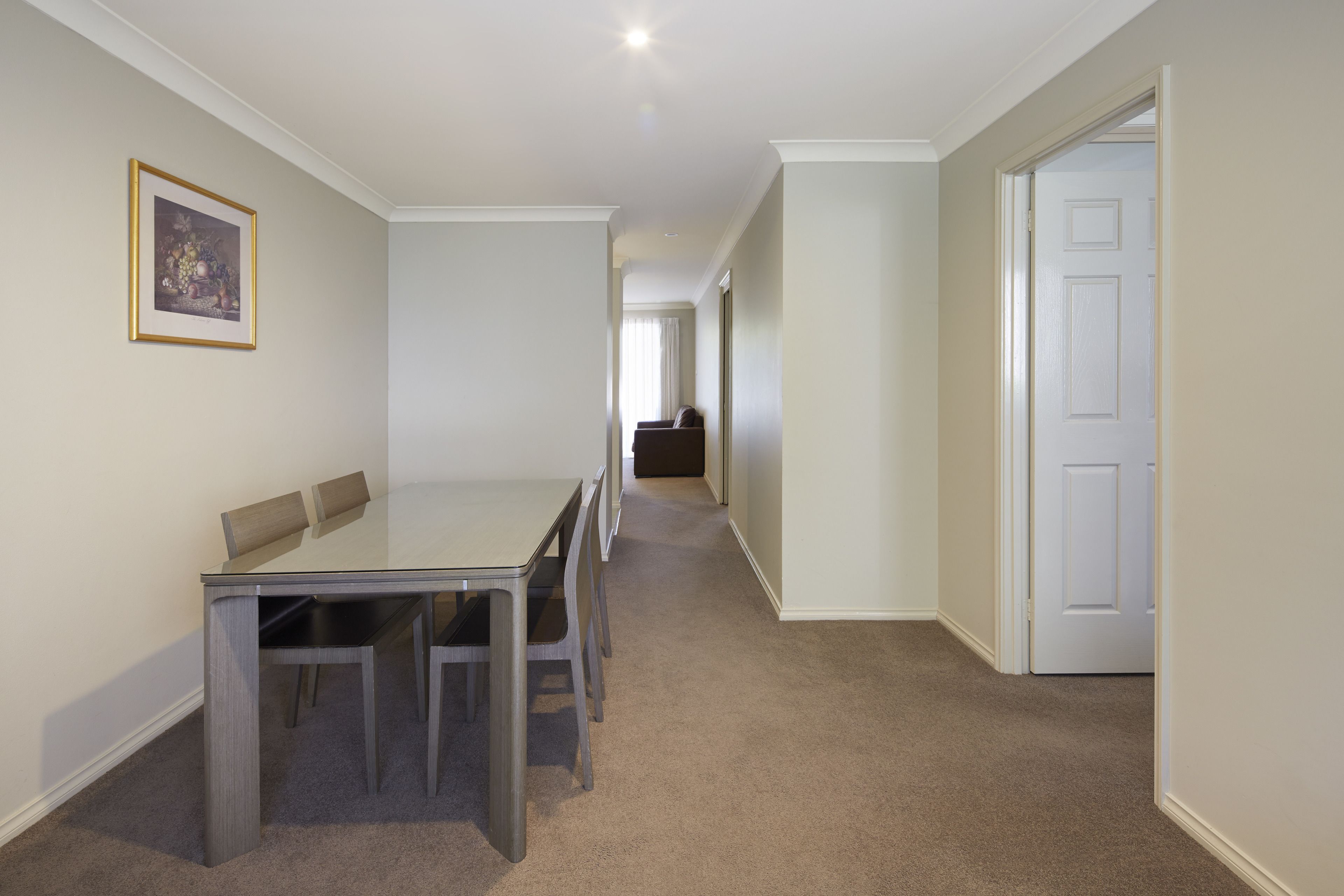 A hallway with a dining area featuring a table and chairs, carpeted flooring, and a framed picture on the wall.
