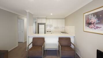 A modern kitchen with white cabinets, a countertop, and a sink. There is a small table with two chairs in the foreground.