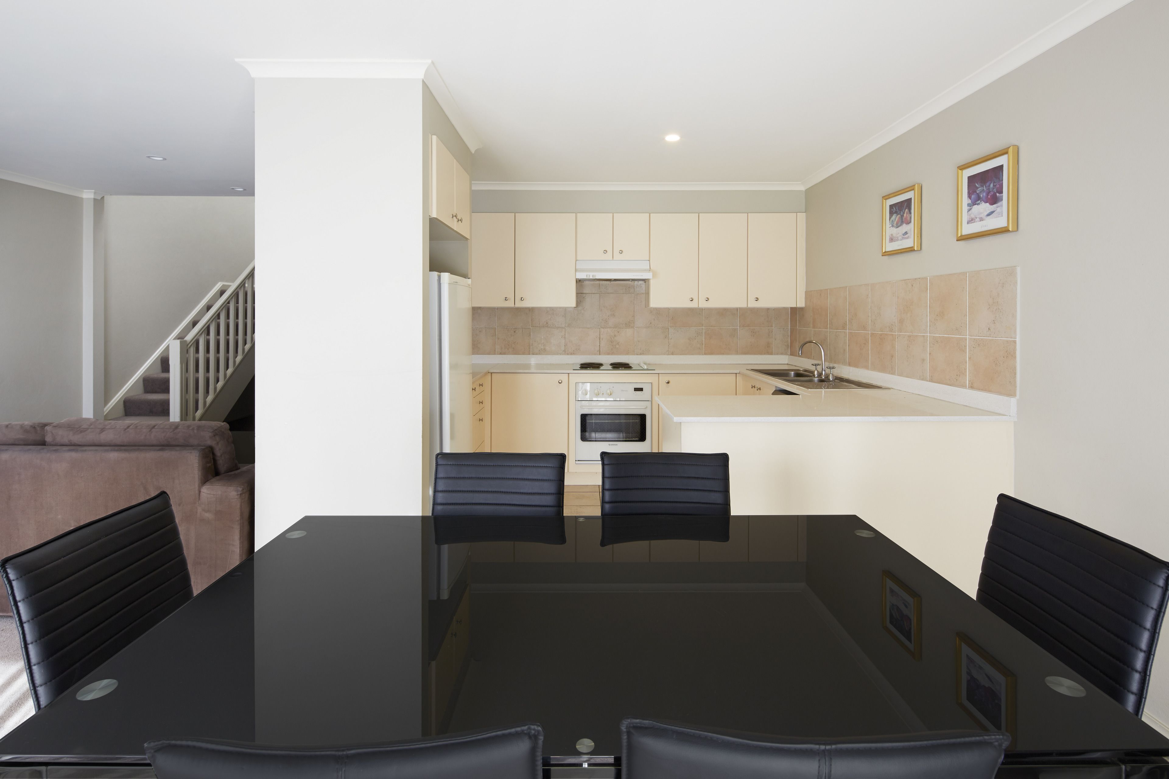 Een moderne keuken met beige kastjes, een eettafel met stoelen, en een trap naar een ander niveau.