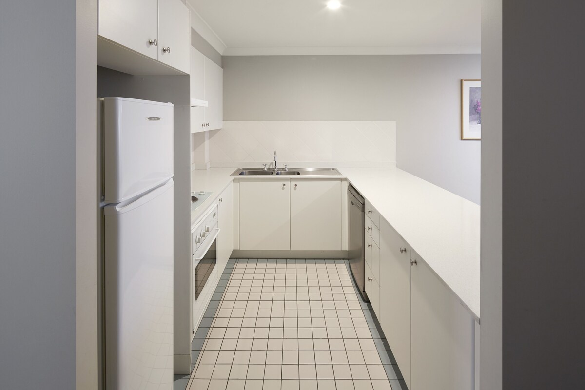 A compact kitchen with white cabinets, a stainless steel sink, and a tiled floor.