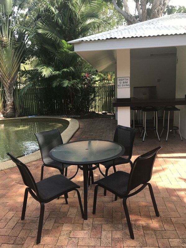 Een terras buiten met een ronde tafel en vier stoelen, een klein zwembad en een overdekte patio met een bord waarop een diepte van 0,8 meter staat aangegeven.