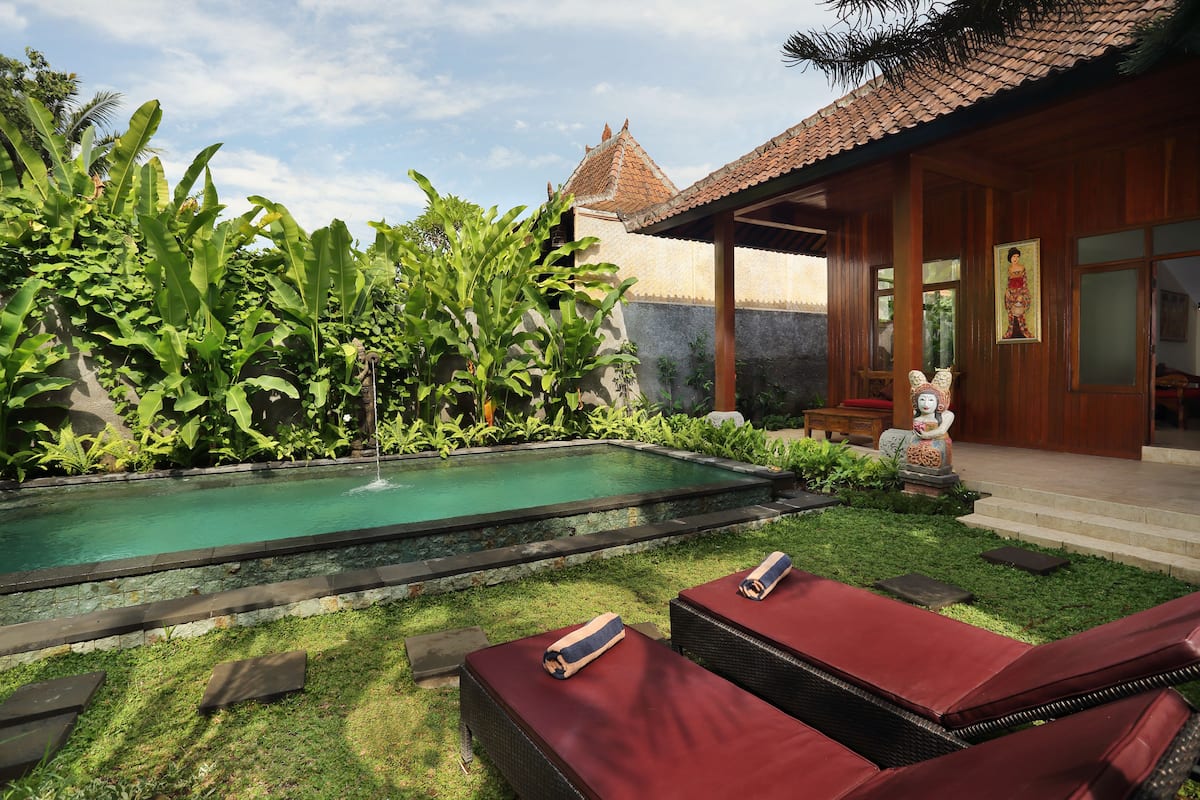 A pool with a fountain, surrounded by lush greenery and red lounge chairs.