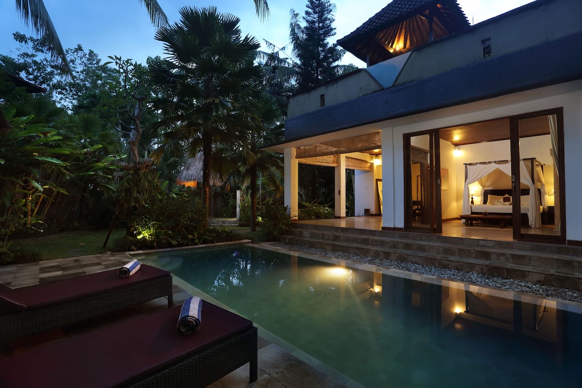 A modern villa with a swimming pool, outdoor seating, and a well-lit interior.