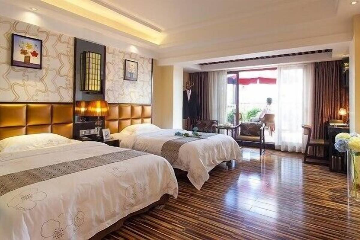A hotel room with two beds, a large window with curtains, a seating area with a table, and a view of the outdoors.