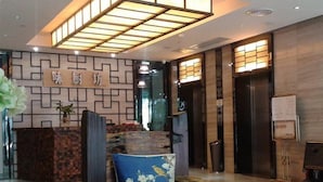 A reception area with a modern design, featuring a reception desk, a seating area with a blue chair, and a wooden bench. - Wellgold Hotel (Guangzhou)