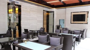 An outdoor seating area with wicker furniture and glass tables, featuring a modern design with a tiled floor and a large window. - Wellgold Hotel (Guangzhou)