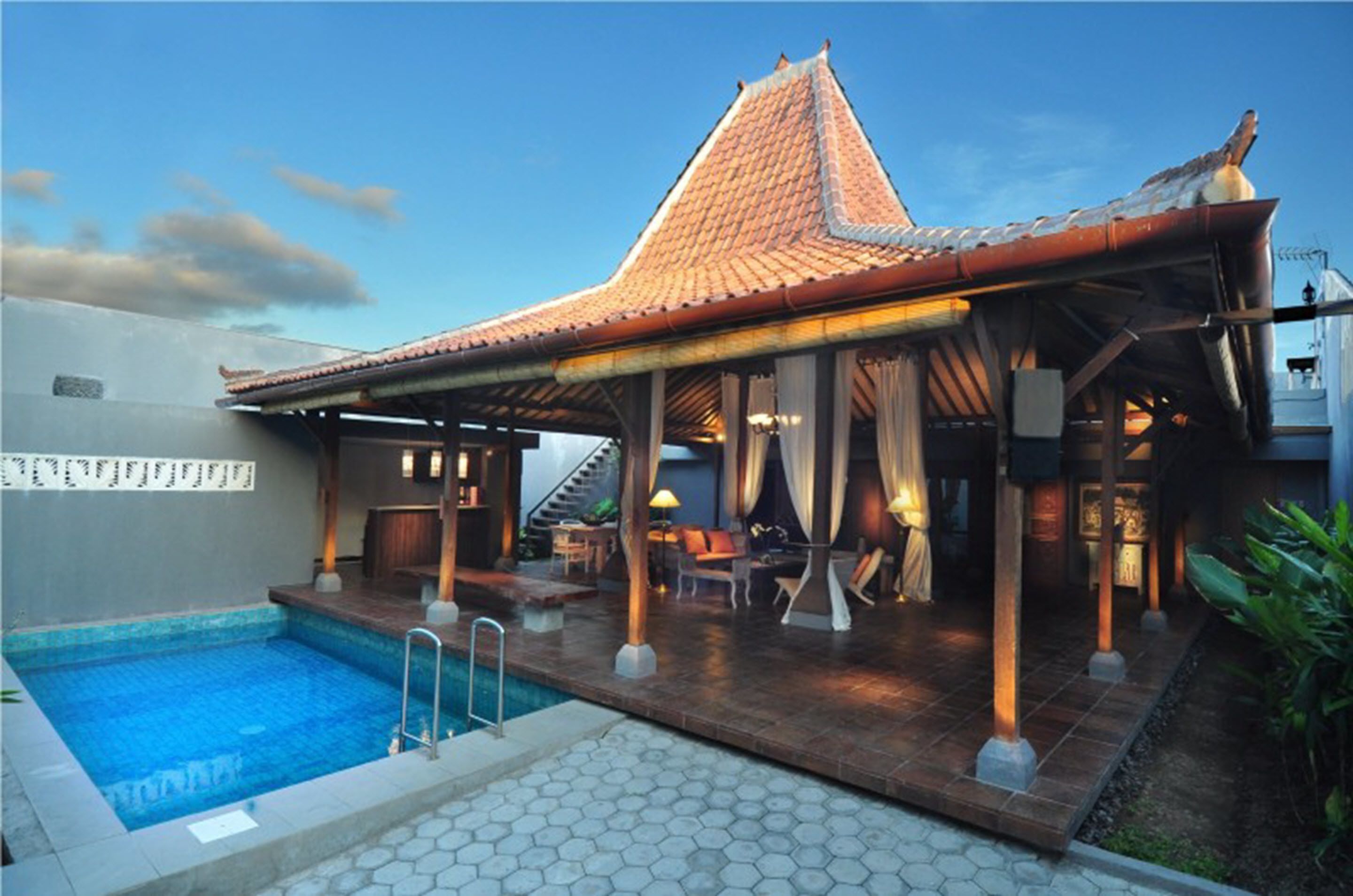 A poolside area with a covered seating area, a swimming pool, and a building with a tiled roof.