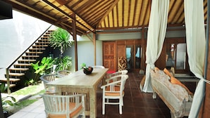 A covered outdoor dining area with a wooden table and chairs, a staircase, and a bench with cushions. - d'Lima Hotel & Villas (Kuta)