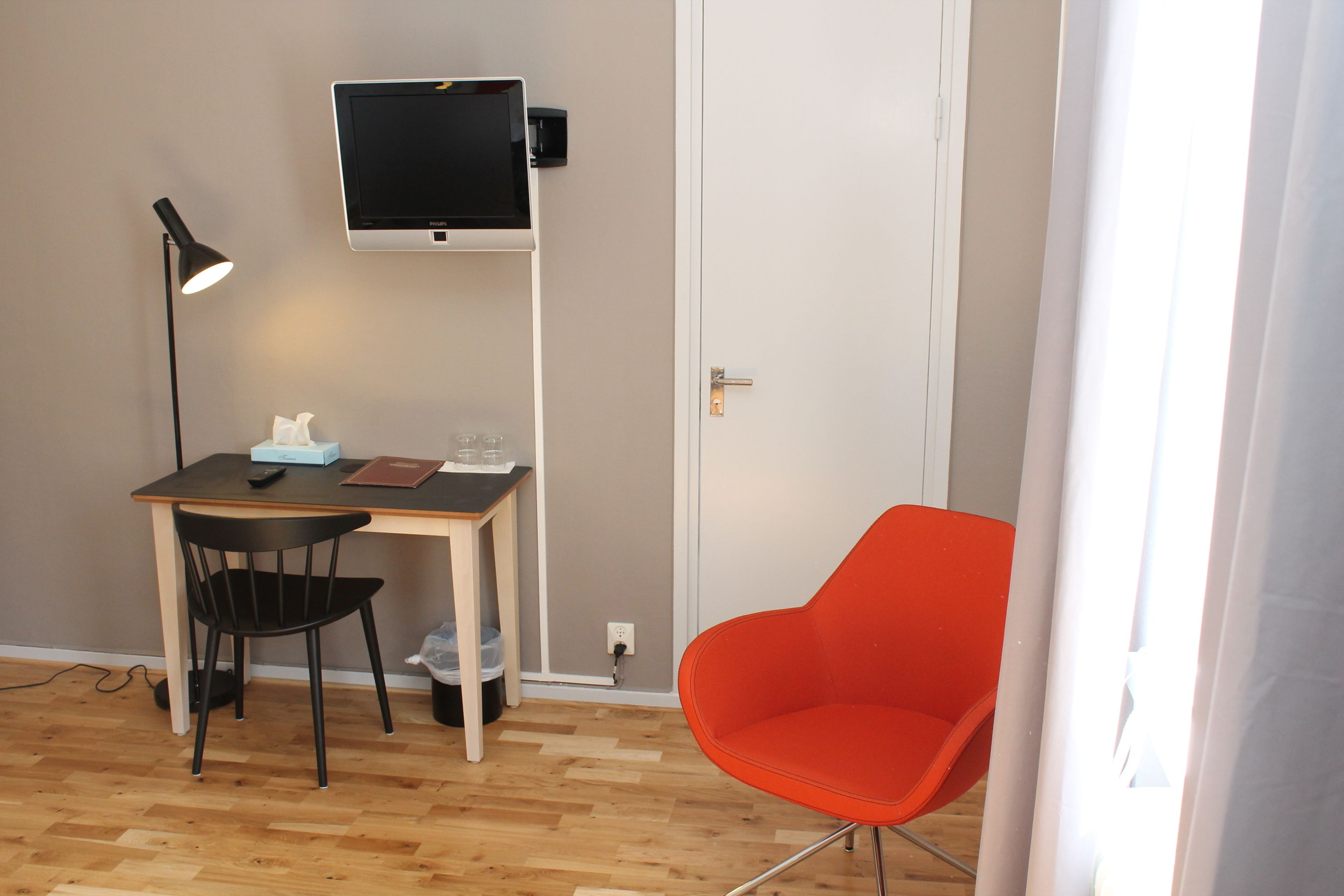 A room with a desk, a chair, a TV mounted on the wall, and a door.