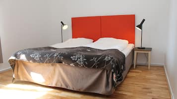 Una cama con colcha estampada, dos lámparas de noche y un cabecero rojo en una habitación con suelo de madera.