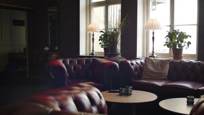 A cozy room with a leather sofa, two round tables, and two potted plants by a window. - Lindesbergs Stadshotell (Lindesberg)