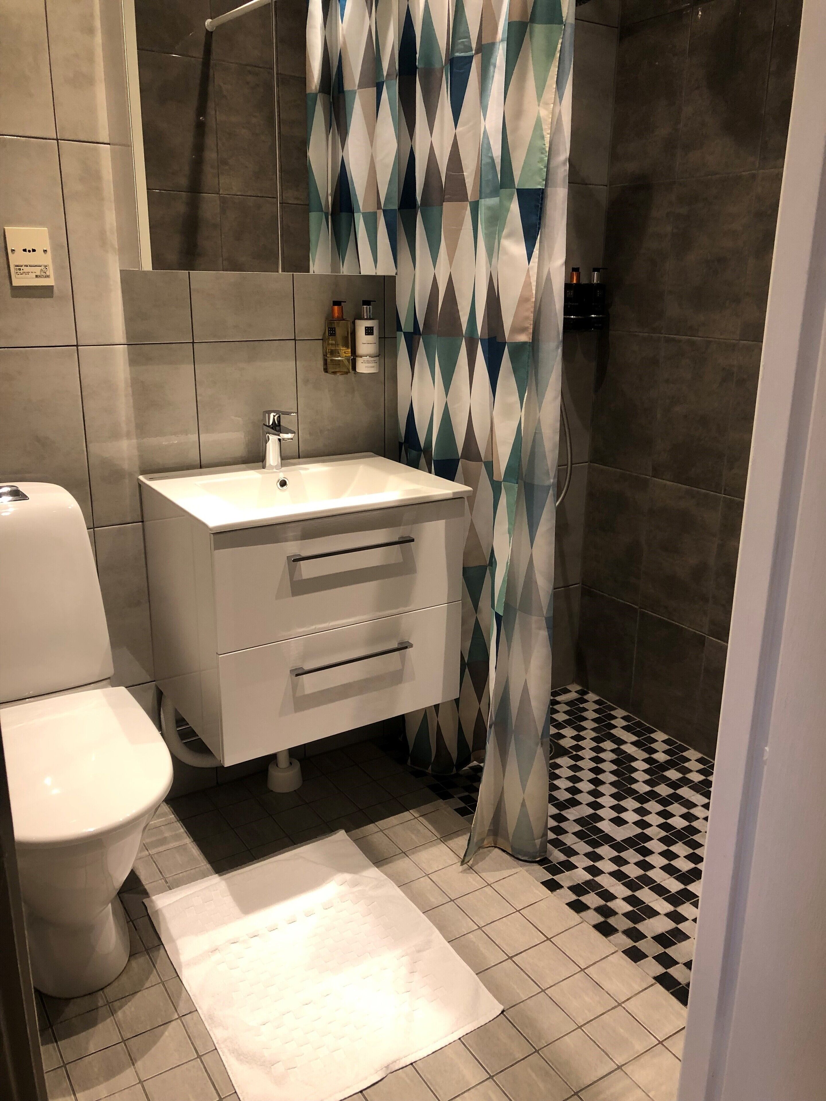A bathroom with a white sink, a toilet, a shower curtain with a geometric pattern, and a checkered floor.