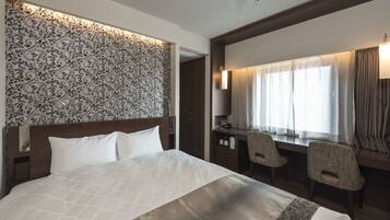 Une chambre d’hôtel avec un grand lit, un bureau avec deux chaises, un mur décoré de motifs et une fenêtre avec des rideaux.