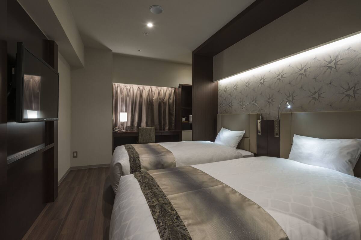 Hotelkamer met twee bedden, een televisie, een badkamer met douchegordijn en een behang met patroon.