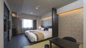 Quarto de hotel com cama, escrivaninha, cadeira, televisão e janela com cortinas.