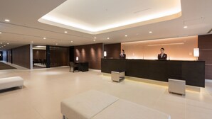 Eine moderne Hotelhalle mit Empfangstresen, Sitzgelegenheiten und einer Treppe zu einer weiteren Etage.