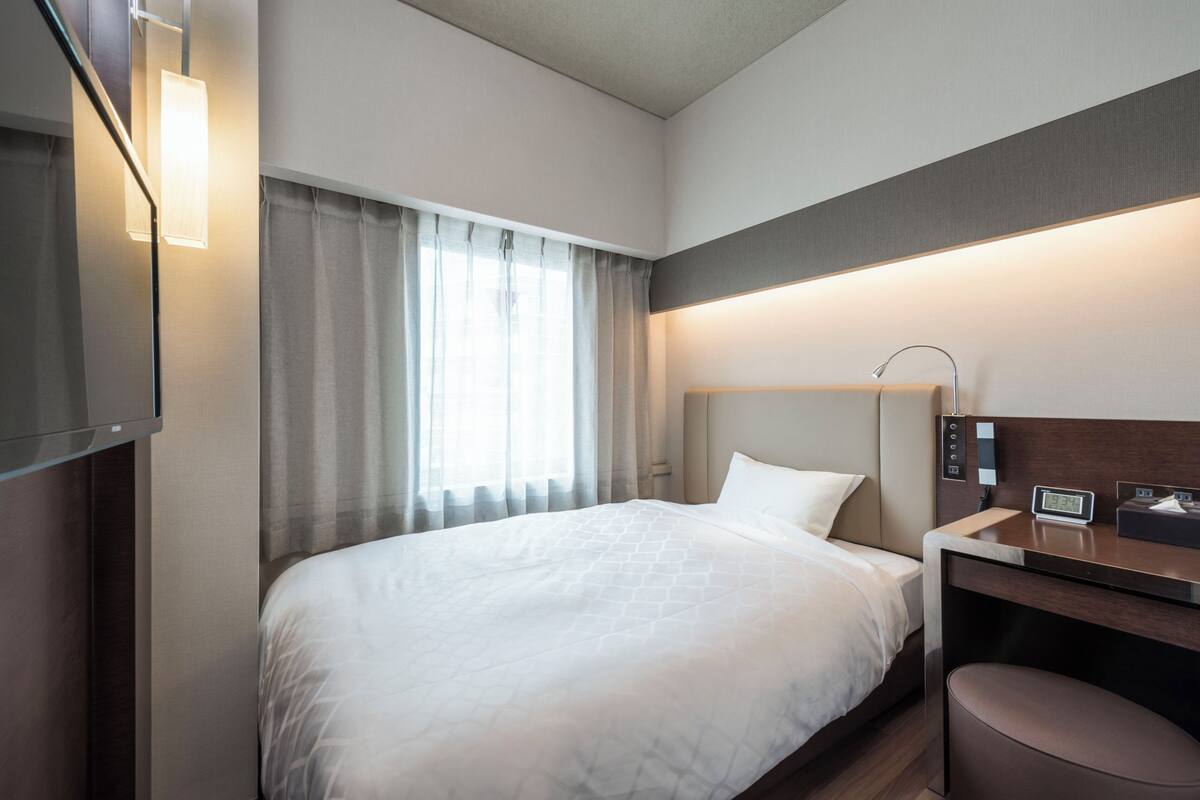 Een hotelkamer met een bed, een bureau, een stoel, een televisie en een raam met gordijnen.