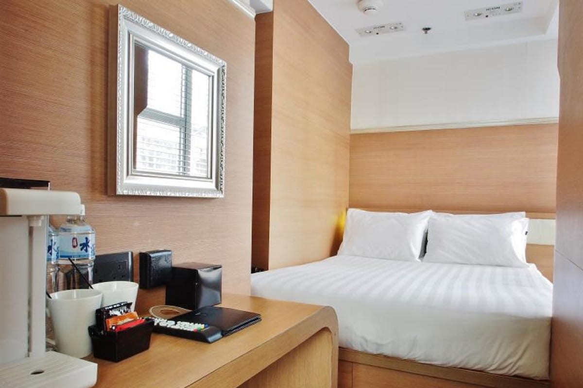 A hotel room with a bed, a desk with a coffee machine, a water bottle, and a remote control.
