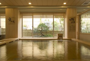 Une pièce spacieuse dotée d'un plancher en bois poli, de grandes portes coulissantes donnant sur un jardin et d'une décoration d'inspiration japonaise traditionnelle.