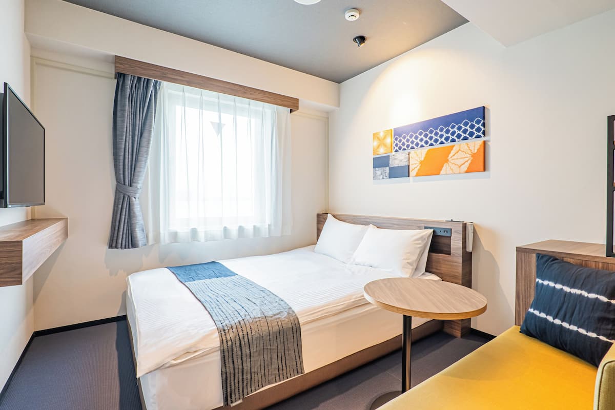 Ein Hotelzimmer mit Bett, einem runden Tisch, einer Couch, einem Fernseher und Kunstwerken an der Wand.