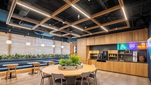 A modern interior with a round wooden table surrounded by chairs, a blue seating area, and a kitchen counter with a neon sign. - -SPA RESORT- Nagoya Kasadera Hotel (Nagoya)